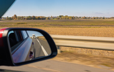 view in the rear view side mirror of a auto, driving a red car along the road