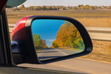 view in the rear view side mirror of a auto, driving a red car along the road