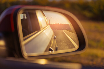 The sun is reflected in the mirror, evening road. View in the rear view side mirror of a auto,...