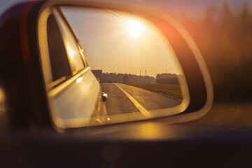 The sun is reflected in the mirror, evening road. View in the rear view side mirror of a auto,...