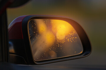 The sun is reflected in the mirror, evening road. View in the rear view side mirror of a auto, driving a red car along the track