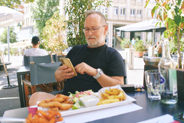  Outdoor portrait of middle age man relaxing in restaurant, using mobile phone