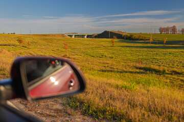 The sun is reflected in the mirror, evening road. View in the rear view side mirror of a auto,...