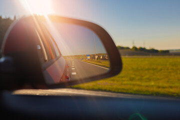 The sun is reflected in the mirror, evening road. View in the rear view side mirror of a auto,...