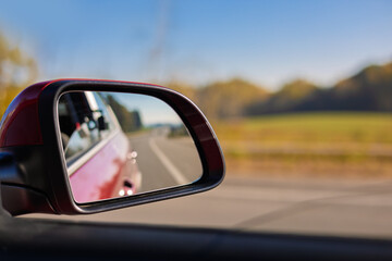 view in the rear view side mirror of a auto, driving a red car along the road