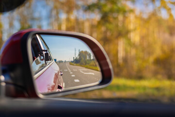 The sun is reflected in the mirror, evening road. View in the rear view side mirror of a auto, driving a red car along the track
