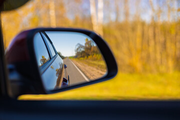 view in the rear view side mirror of a auto, driving a red car along the road