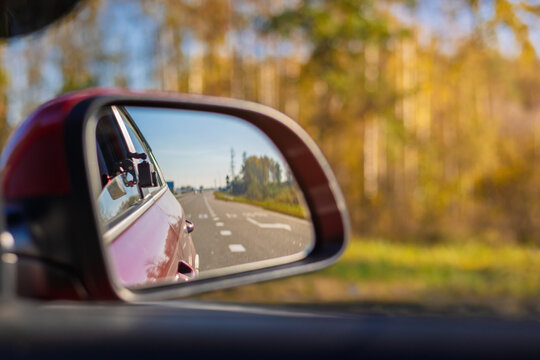 The sun is reflected in the mirror, evening road. View in the rear view side mirror of a auto, driving a red car along the track