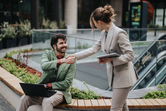 A business interaction occurs outdoors as two colleagues exchange a handshake, displaying professionalism and collaboration in a modern urban setting.