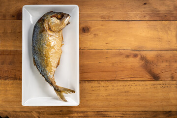 Fried mackerel on a white plate placed on a wooden surface,Traditional Thai Golden-brown fried fish (mackerel) on a white plate on wood surface.