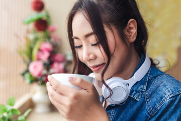 Close-up portrait of happy young woman listening to music with headphones and drinking coffee in coffee shop