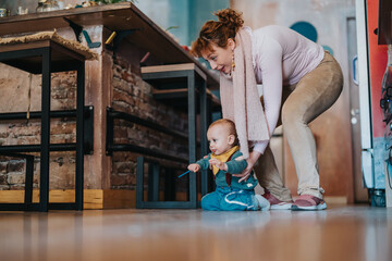 A parent supports their child while they explore movement on a wooden indoor floor, showcasing...