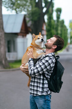 Portrait of a young man holding and kissing shiba inu dog in arms during summer park walk affectionate moment pet companionship concept love outdoor