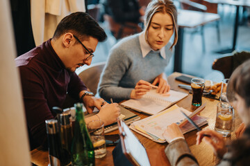 A group of professionals engaged in a collaboration session, planning strategies over notes in a casual business meeting atmosphere in a modern cafe.