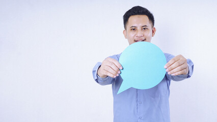 A man holding blank round blue paper speech bubble in front of his chest isolated on white...