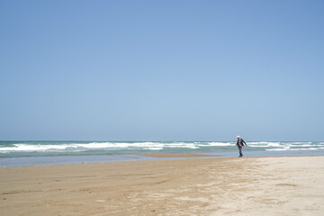 Fototapeta premium On a sunny May day by the Sea of Japan, a Japanese man in his late 70s wearing a checkered shirt and gray jacket spends time alone on the beach. Gentle waves and spring air create a peaceful mood.