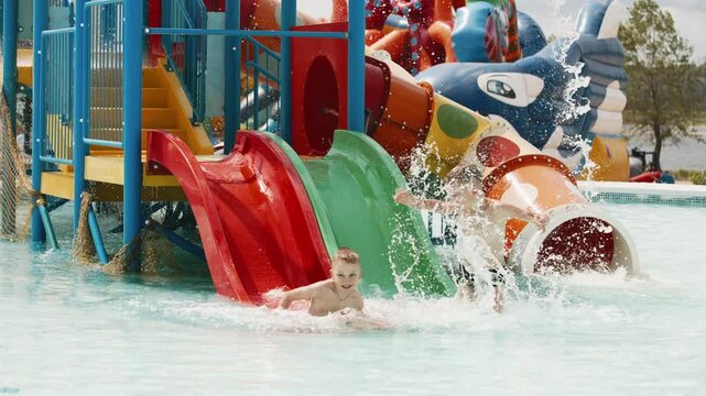 Two children boys sliding down water slide in kiddie pool. Summer vacation concept.