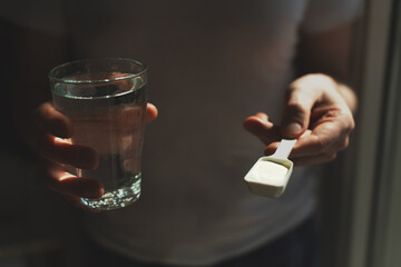 Man hands with a scoop with collagen or protein powder and a glass of water. Trendy beauty supplement for healthy skin and bones.