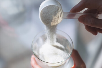 Woman hands with a scoop pouring collagen or protein powder in a glass of water. Trendy beauty supplement for healthy skin and bones.
