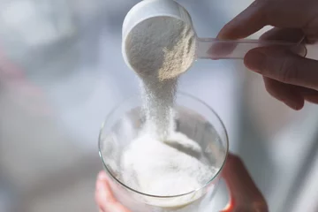 Woman hands with a scoop pouring collagen or protein powder in a glass of water. Trendy beauty supplement for healthy skin and bones. © Yulia Lisitsa