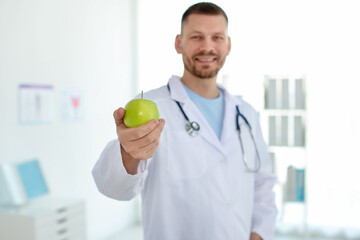 Nutritionist with green apple and stethoscope in clinic, selective focus