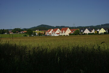 A residential area with uniform houses and red roofs set against green hills. This countryside...