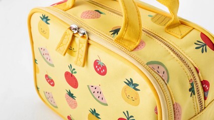 Close-up of a bright yellow kids’ lunch bag with a fun fruit pattern, focusing on the handle and zipper area, on a white background