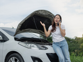 An upset woman is talking on the phone to a broken car with the hood open.