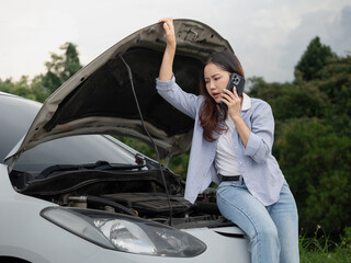 An upset woman is talking on the phone to a broken car with the hood open.