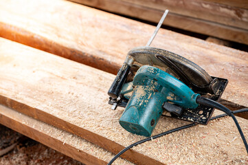 Electric circular saw on timber stack. Work tool for carpentry in a wood workshop used for cutting wooden plank. Lumber industry concept