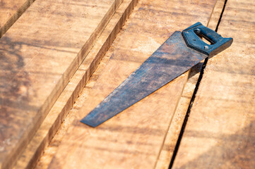 Rustic old hand saw on timber stack at construction site. Work tool for cutting in lumber industry