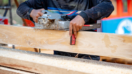 Male carpenter hand using angle ruler for wood squaring and planing on wooden plank by electric planer on workbench in workshop. Wood measuring and shaving process for lumber industry