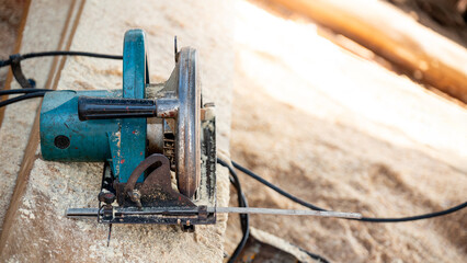 Electric circular saw on timber stack in a wood workshop. Work tool for carpentry used for cutting wooden plank or board. Lumber industry concept