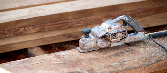 Rustic old electric planer on timber stack or wooden plank with sawdust spreading around. Work tool for carpentry. Lumber industry concept