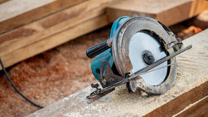 Electric circular saw on timber stack in a wood workshop. Work tool for carpentry used for cutting wooden plank or board. Lumber industry concept
