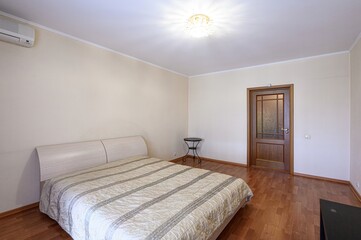 tidy bedroom with a bed, wooden floors, and a door. The walls are pale yellow, and a crystal chandelier hangs from the ceiling