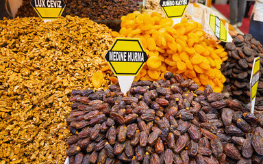 Assortment of dried fruits and nuts for sale at bustling market. Displays feature dates, apricots, and walnuts, showcasing traditional Turkish market scene. Food background.