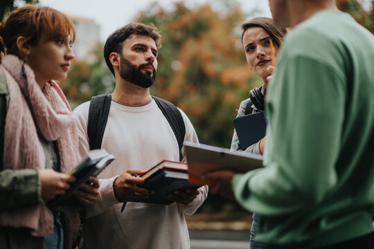 A group of students engaging in a lively discussion outdoors, surrounded by autumn foliage. They are carrying books and notebooks, sharing ideas and collaborating on a project. - Powered by Adobe