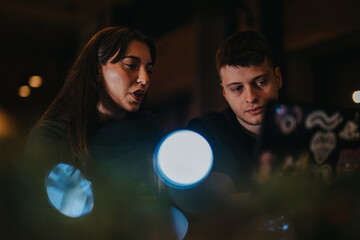 Two people sit together working collaboratively on a project, illuminated by artistic lighting in a cozy environment. The setting suggests focus, collaboration, and creativity in their task.