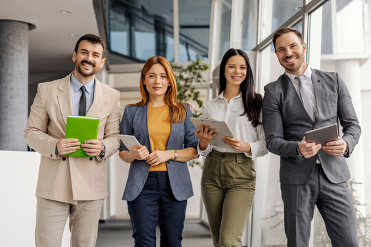 Gender balanced leadership team standing at corporation in a lobby and smiling at camera.