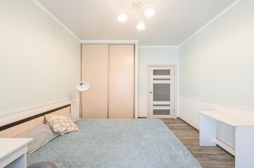 bright, clean bedroom with light blue walls, a bed with a blue blanket, a sliding door closet, and a white desk