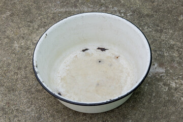 Worn enameled white basin with black rim on concrete ground outdoors