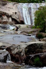 Paisaje de hombre caminando por el cauce de un río con cascada de agua al fondo 