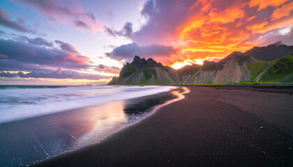 Vibrant sunset over a dramatic mountain landscape with a dark sandy beach in the foreground
