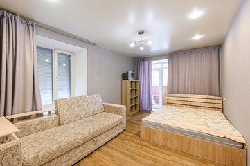 Cozy room with a patterned sofa, wooden bed, and light purple curtains. Simple decor, bright lighting.
