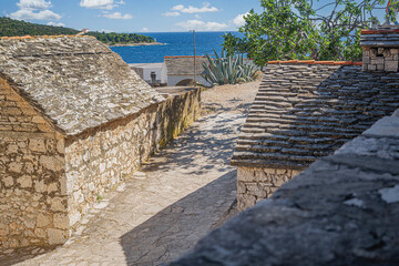 A quiet, sunlit street in the old town of Primosten, Croatia, lined with traditional stone buildings and Mediterranean charm.