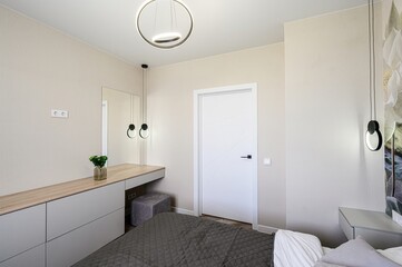 bedroom interior featuring modern furniture, including a grey dresser, a white door with geometric patterns, and stylish lighting fixtures