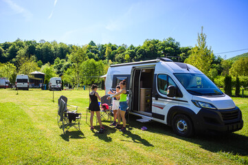 Family camping with a campervan in a campsite in Bosnia near Una River. Family relaxing with camper van, chairs and table on vacation, applying sunscreen before hike.