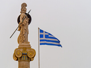 Marble statue of Athena, the Greek Goddess of wisdom and science, on an Ionic column beside the Greek flag in Athens, Greece. Space for your text and logo.