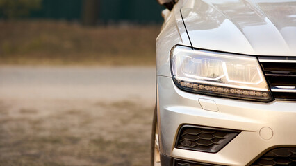 Modern crossover car SUV detailing. Close up shot of front part with bumper engine hood radiator grille and headlight 16x9 rural banner background with copy space.